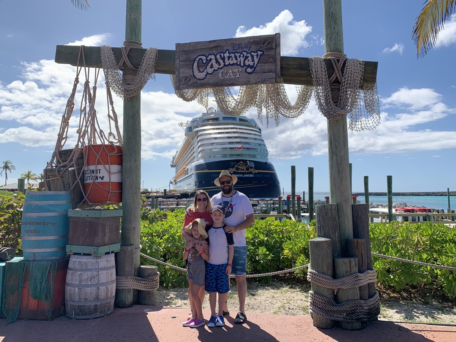 A family under the Castaway Cay sign, the ship docked behind them