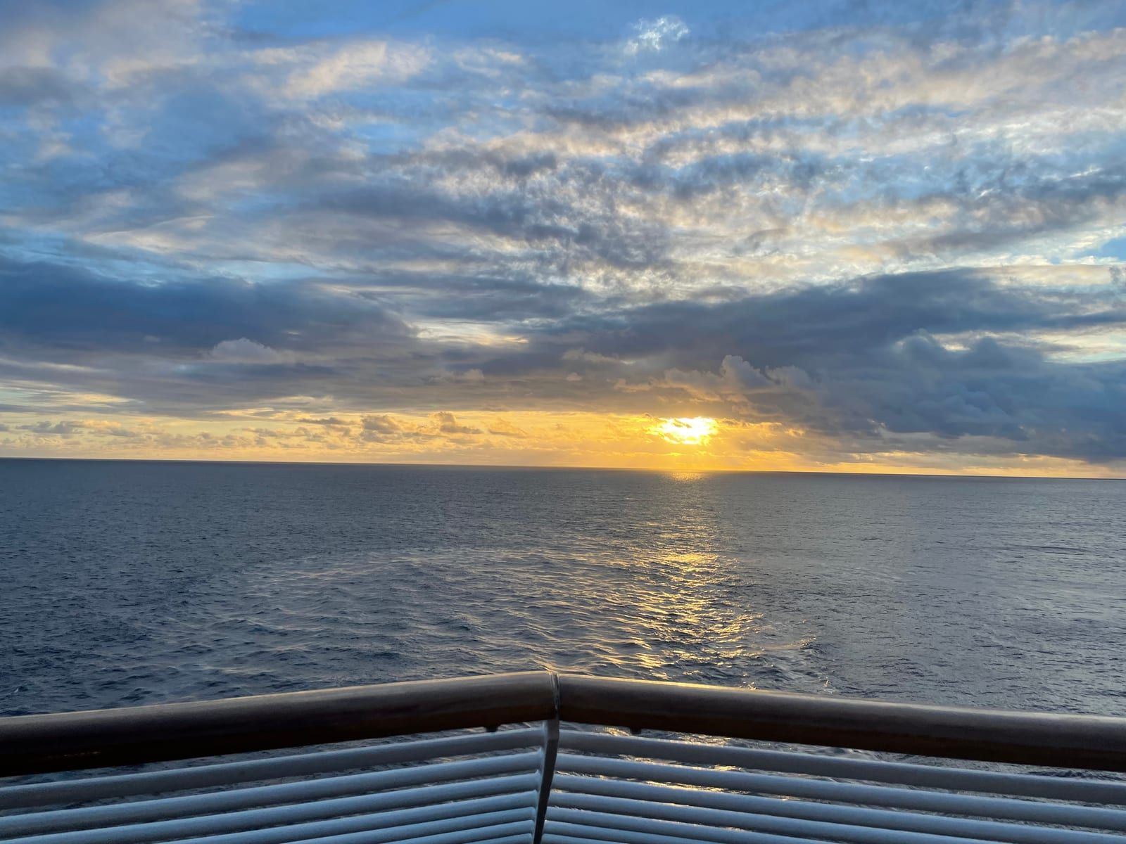 Sunset over a calm Atlantic from the ship's aft rail, the wake trailing away behind